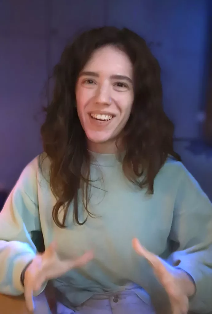 young person with beaming smile and long dark hair waving at the camera with both hands